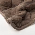 Detail van het gewatteerde bloemmotief op de taupe bedsprei
