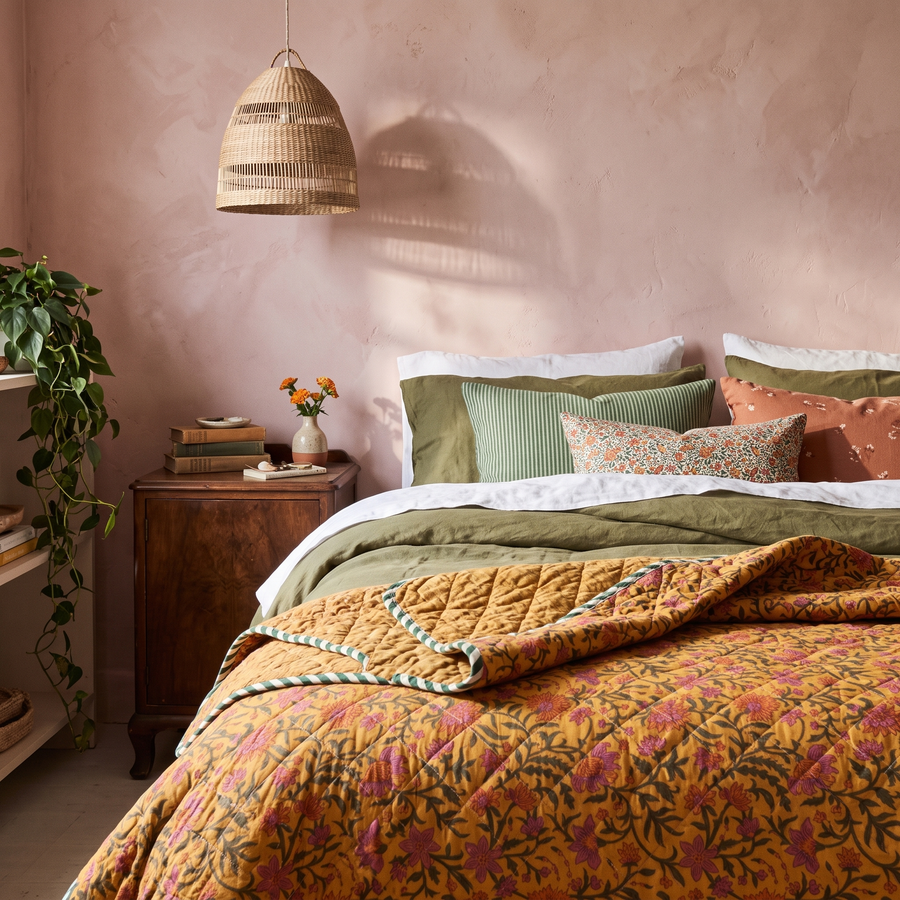 Bloemenquilt okergeel aan het voeteneind van het bed in een kleurrijke slaapkamer