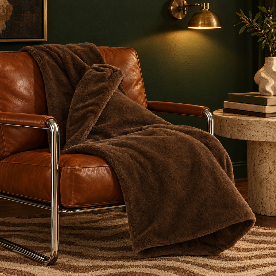 Fleece plaid bruin over een cognac leren fauteuil voor een groene muur