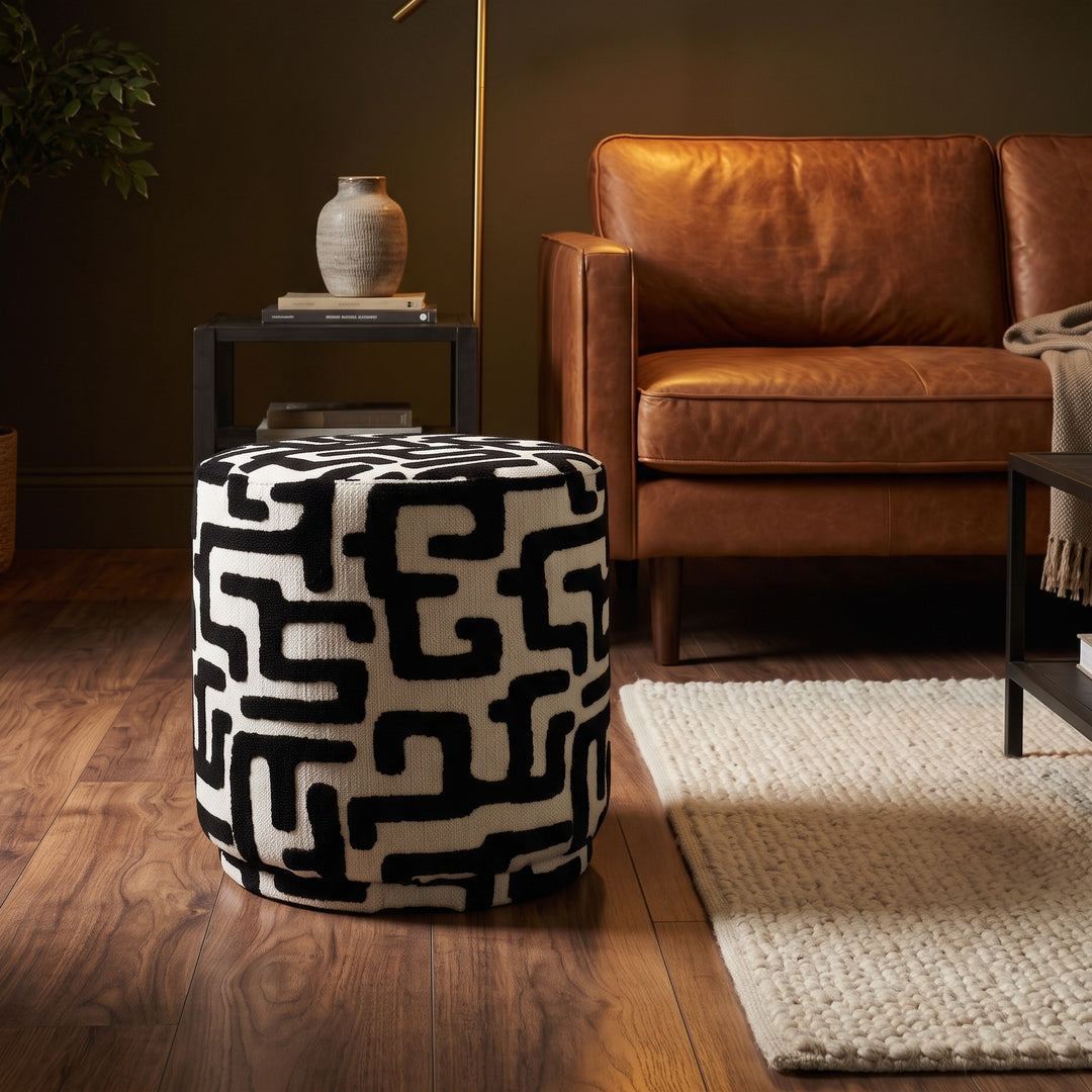 Ronde poef met doolhofprint zwart wit naast cognac leren bank